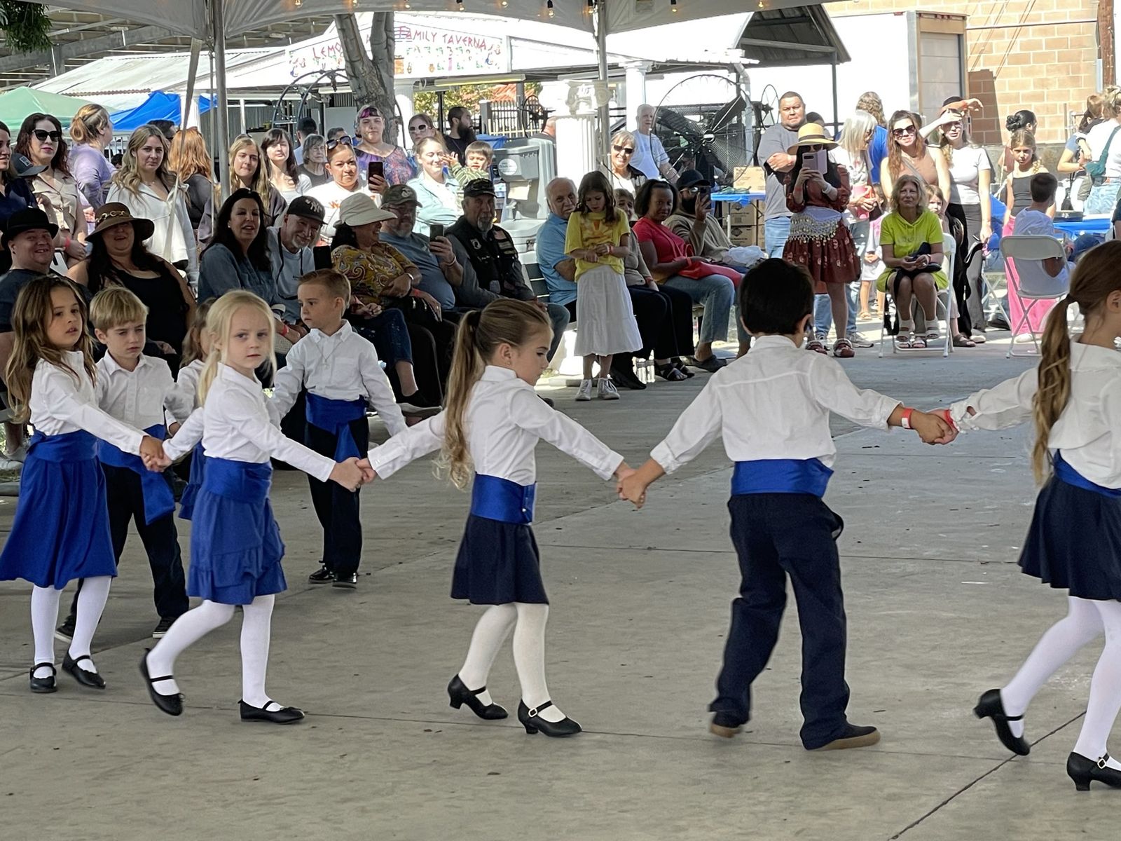 Children in white shirts and blue sashes dancing in a circle