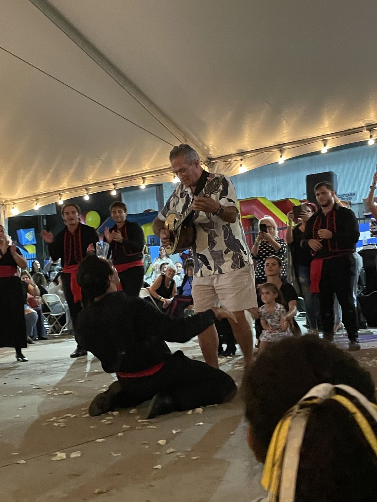 Musician playing guitar beside a kneeling dancer under the tent