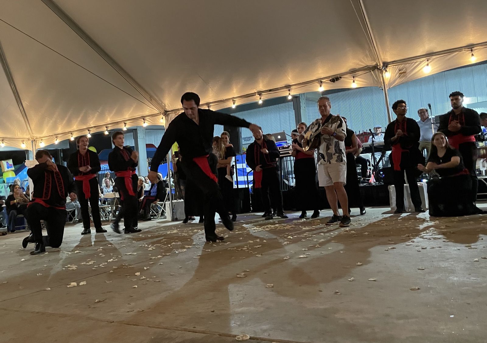 Men in black with red sashes dancing under the festival tent