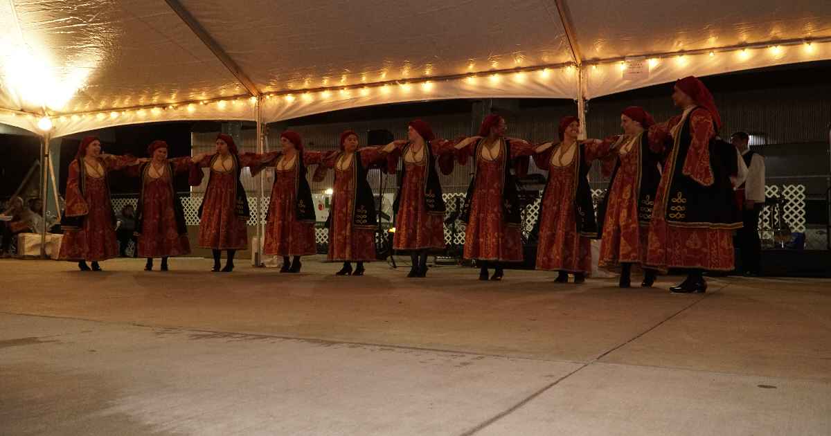 Women in traditional red and gold dress dancing in a line under the tent
